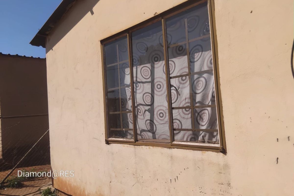 Exterior view of a residential building featuring a metal-framed window with security burglar bars and plastered wall finish.