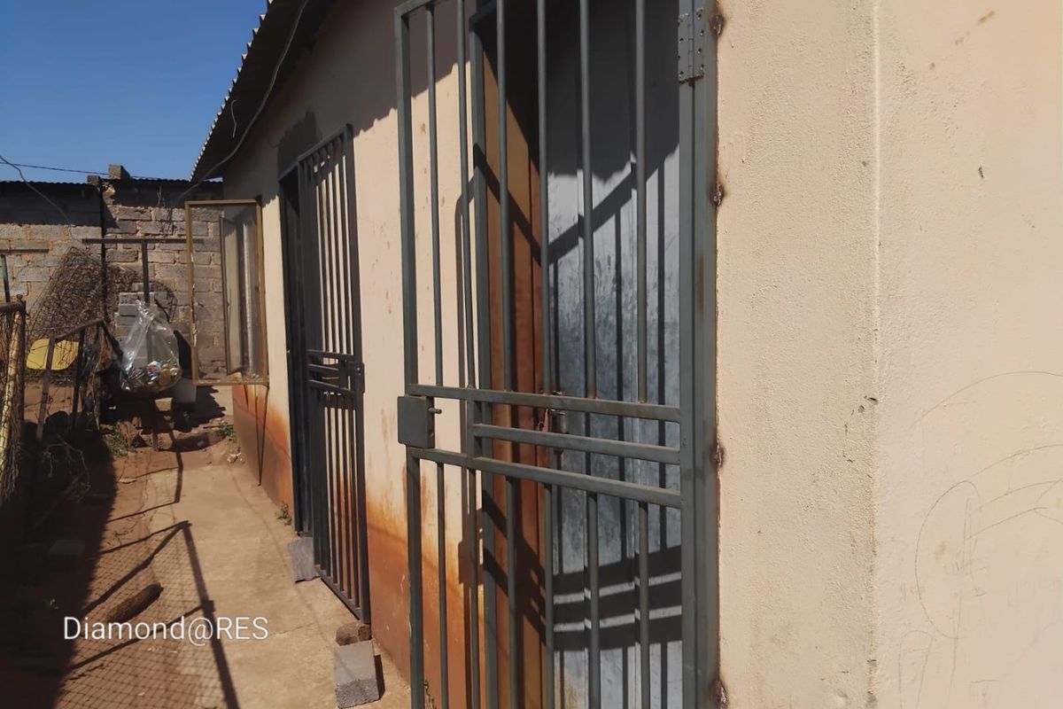 Exterior view of the rear of the property featuring security gates and a concrete pathway along the building wall.