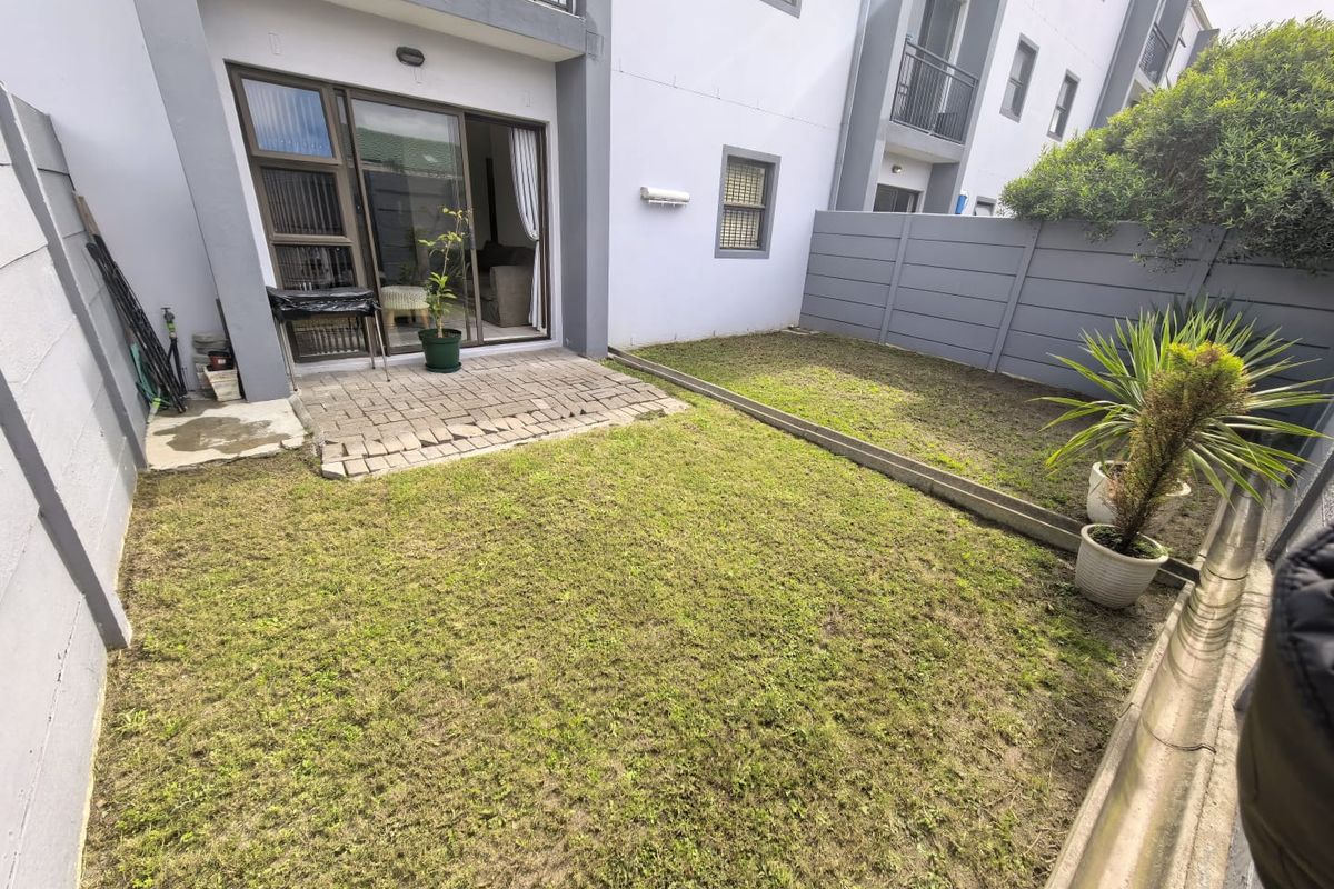 Private rear garden featuring a paved patio area and enclosed boundary walls, accessible via sliding glass doors from the apartment living space.