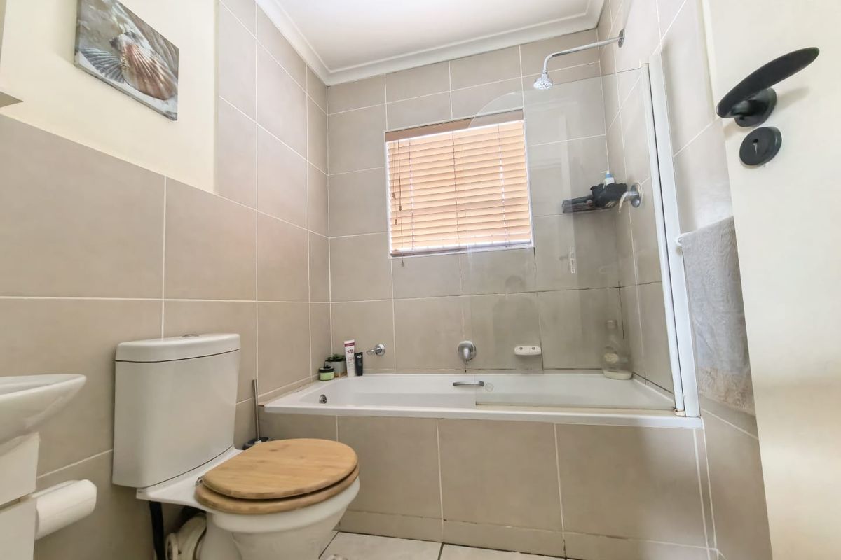 A functional bathroom featuring a built-in bathtub with an integrated shower, glass screen, neutral wall tiles, and a toilet.