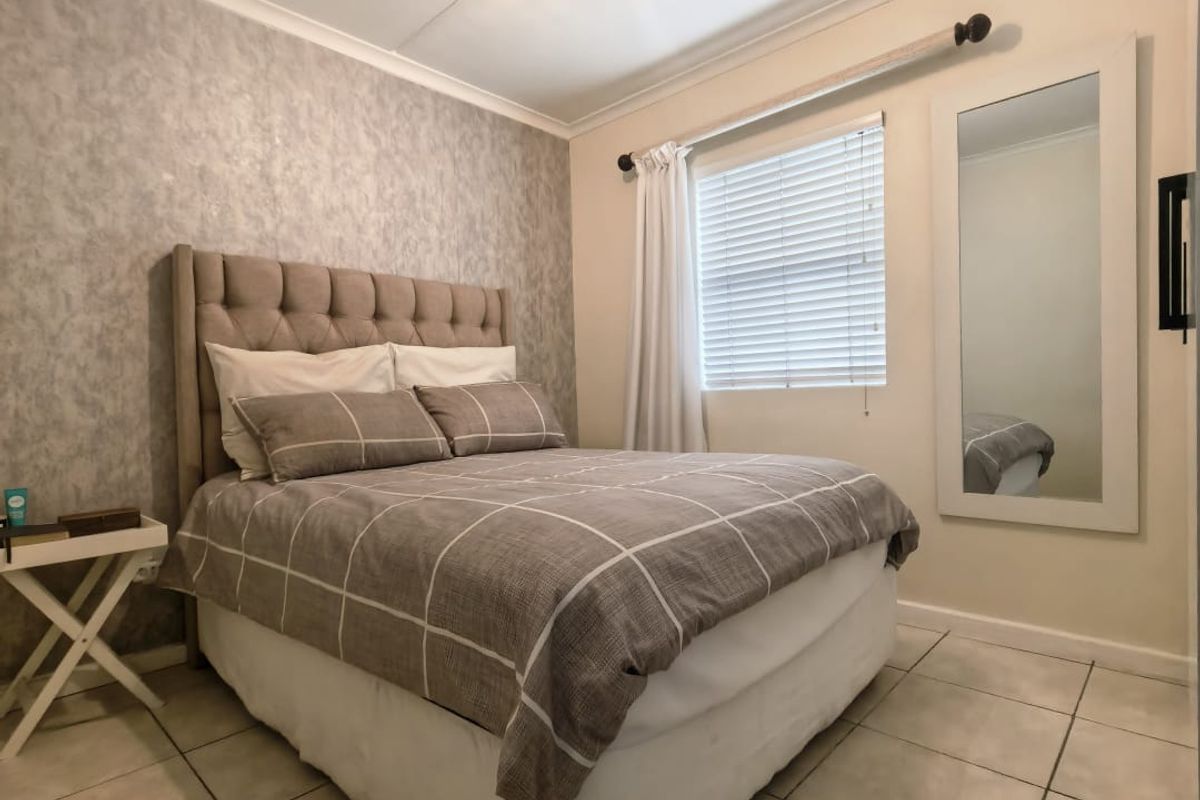 A well-maintained bedroom featuring neutral tiled flooring, a textured feature wall, and venetian blinds for natural light control.