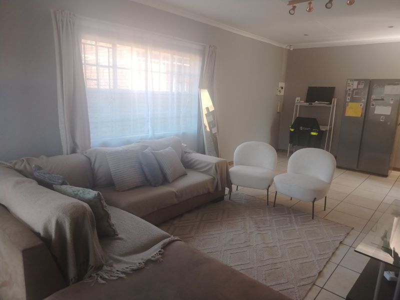 A neutrally painted living room featuring tiled flooring and a large window with security bars, offering a functional and well-lit living space.
