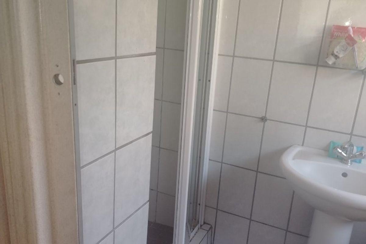 A functional bathroom featuring a pedestal washbasin and a shower enclosure with tiled walls and flooring, currently showing signs of wear.