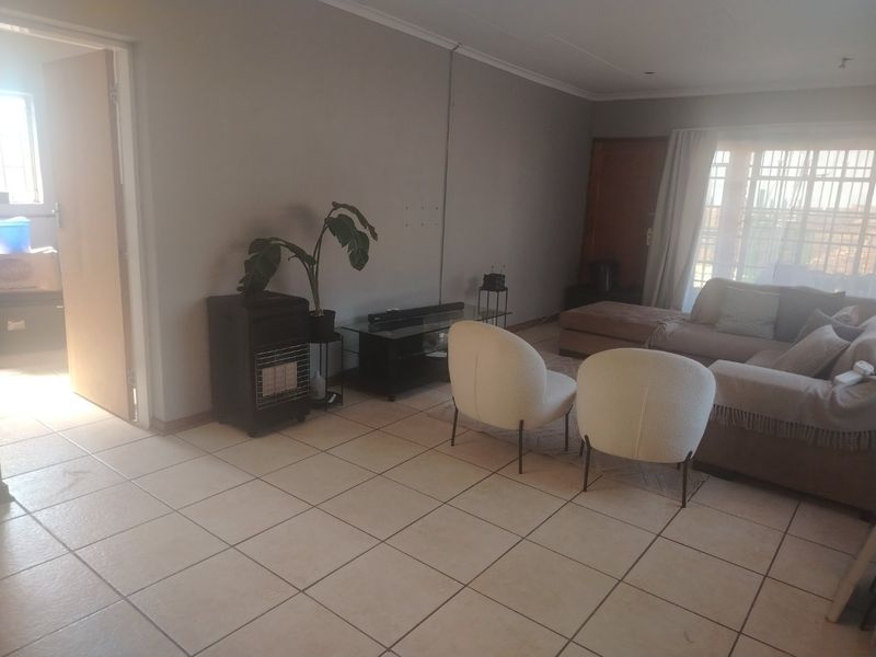 A living room area featuring neutral tiled flooring and large windows with security bars, offering a functional space with potential for cosmetic updates.