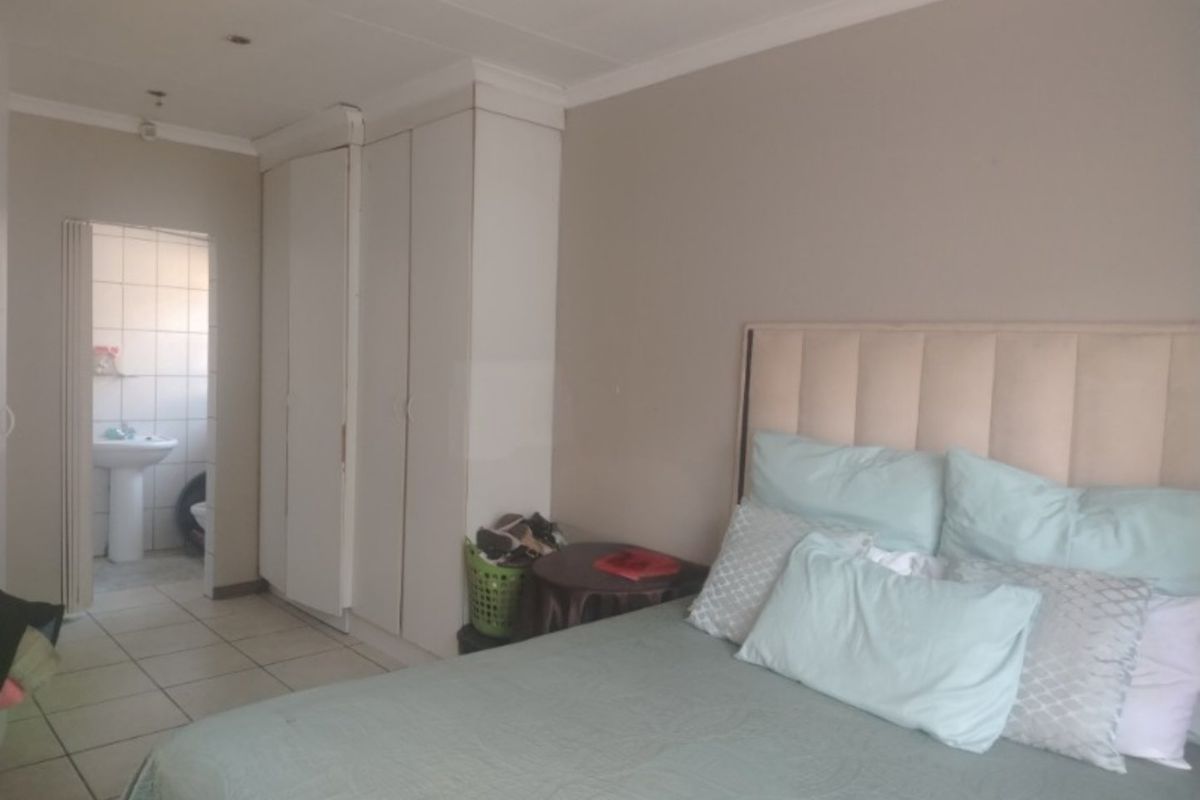 A bedroom featuring built-in cupboards, tiled flooring, and recessed ceiling lights, with an adjoining bathroom visible through the doorway.