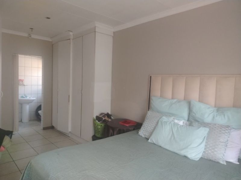 A bedroom featuring built-in cupboards, tiled flooring, and recessed ceiling lights, with an adjoining bathroom visible through the doorway.