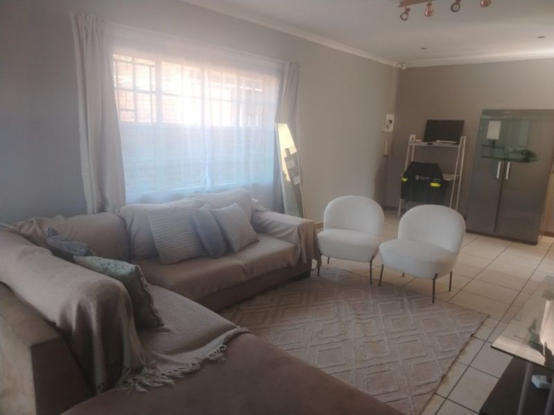 A living room featuring tiled flooring and a window with security bars, providing a functional and neutral space.
