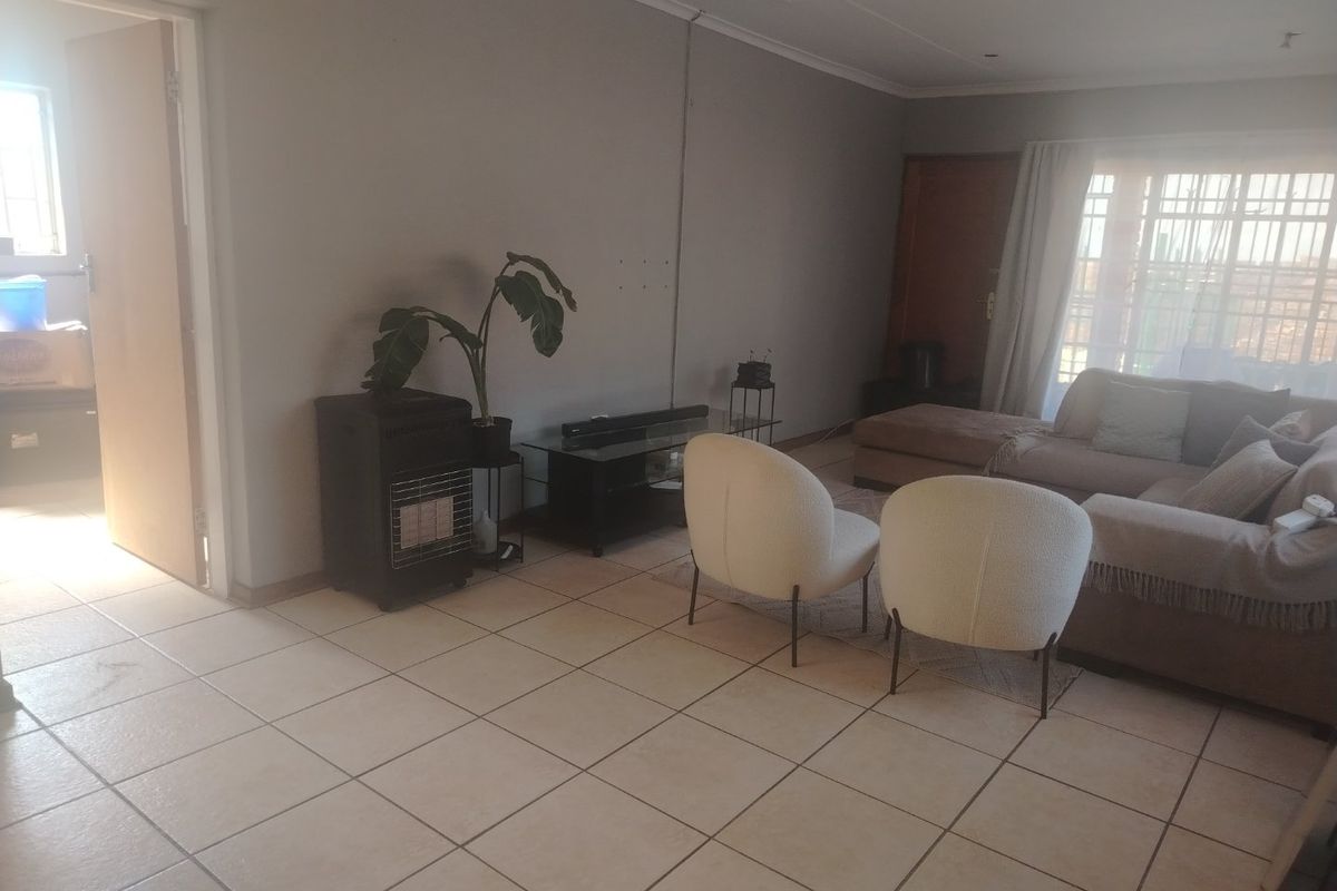 A living room area featuring neutral tiled flooring and large windows with security bars, offering a functional space with potential for cosmetic updates.