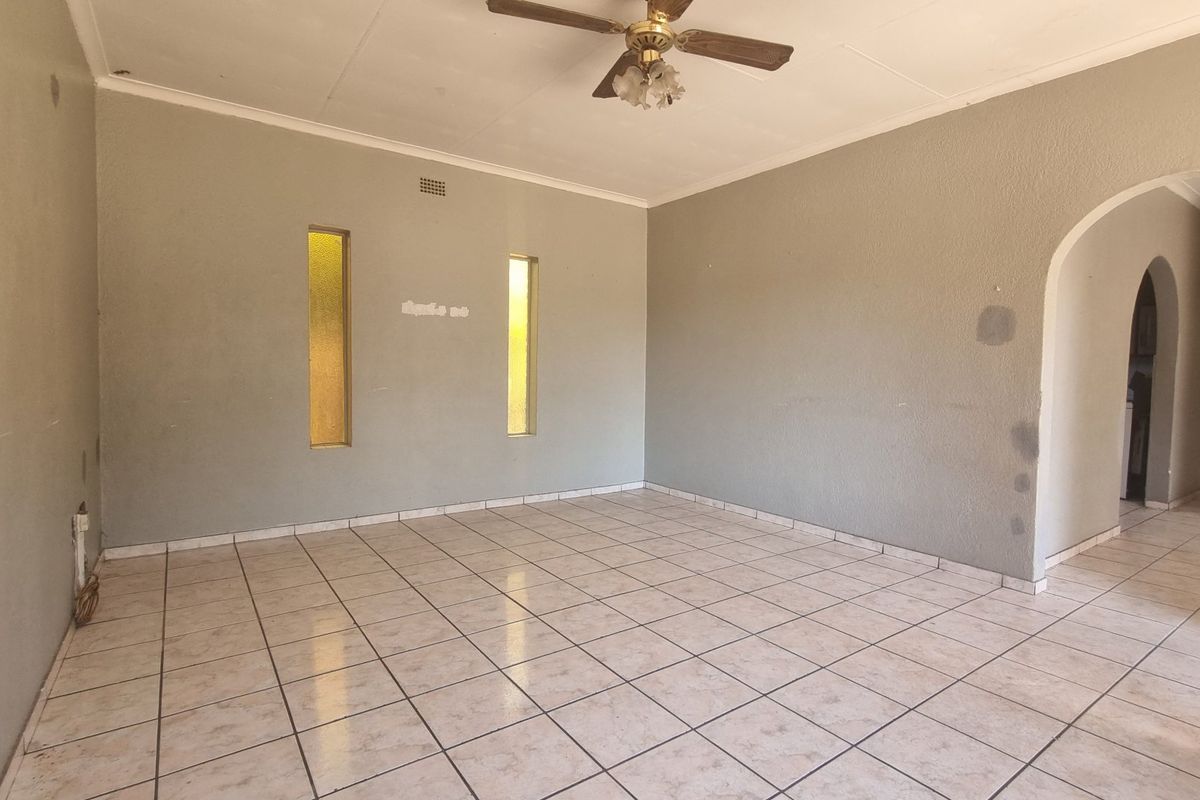 An empty living room featuring tiled flooring, a ceiling fan, and distinctive vertical slit windows, leading into an adjacent space through an arched doorway.