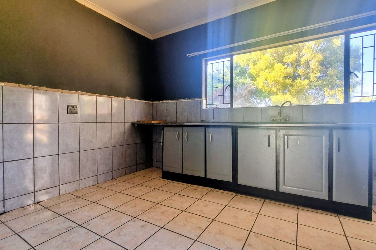 A functional kitchen space featuring tiled flooring, built-in cabinetry, and a sink, awaiting cosmetic updates to complete the wall finishes.
