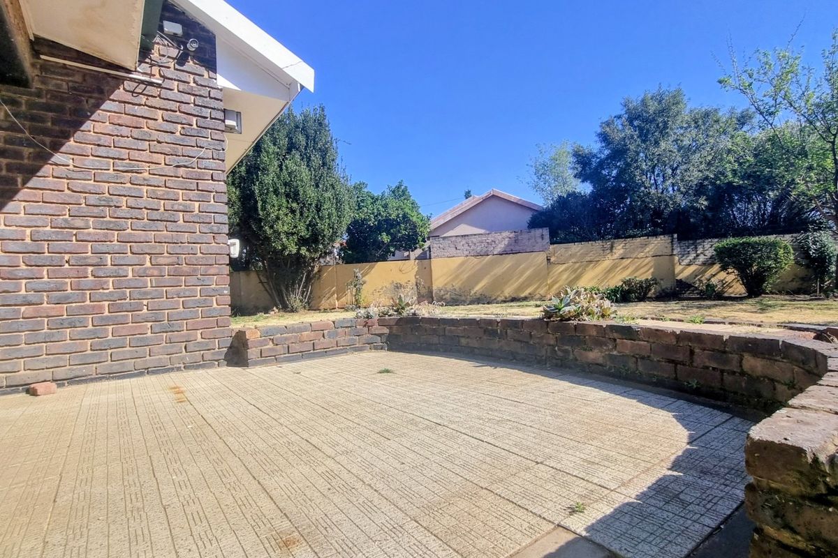 A rear exterior view featuring a paved patio area, a low brick retaining wall, and a perimeter boundary wall in a garden setting.