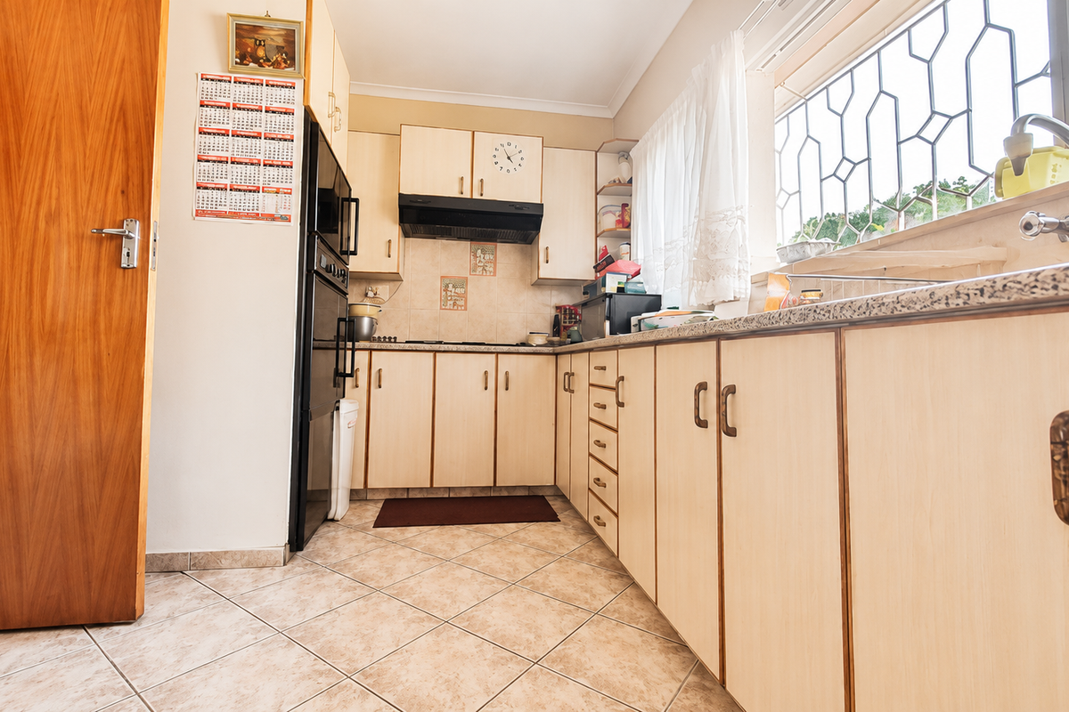 A functional kitchen featuring built-in cabinetry, laminate countertops, a built-in oven, extractor fan, and ceramic tile flooring with security bars on the window.