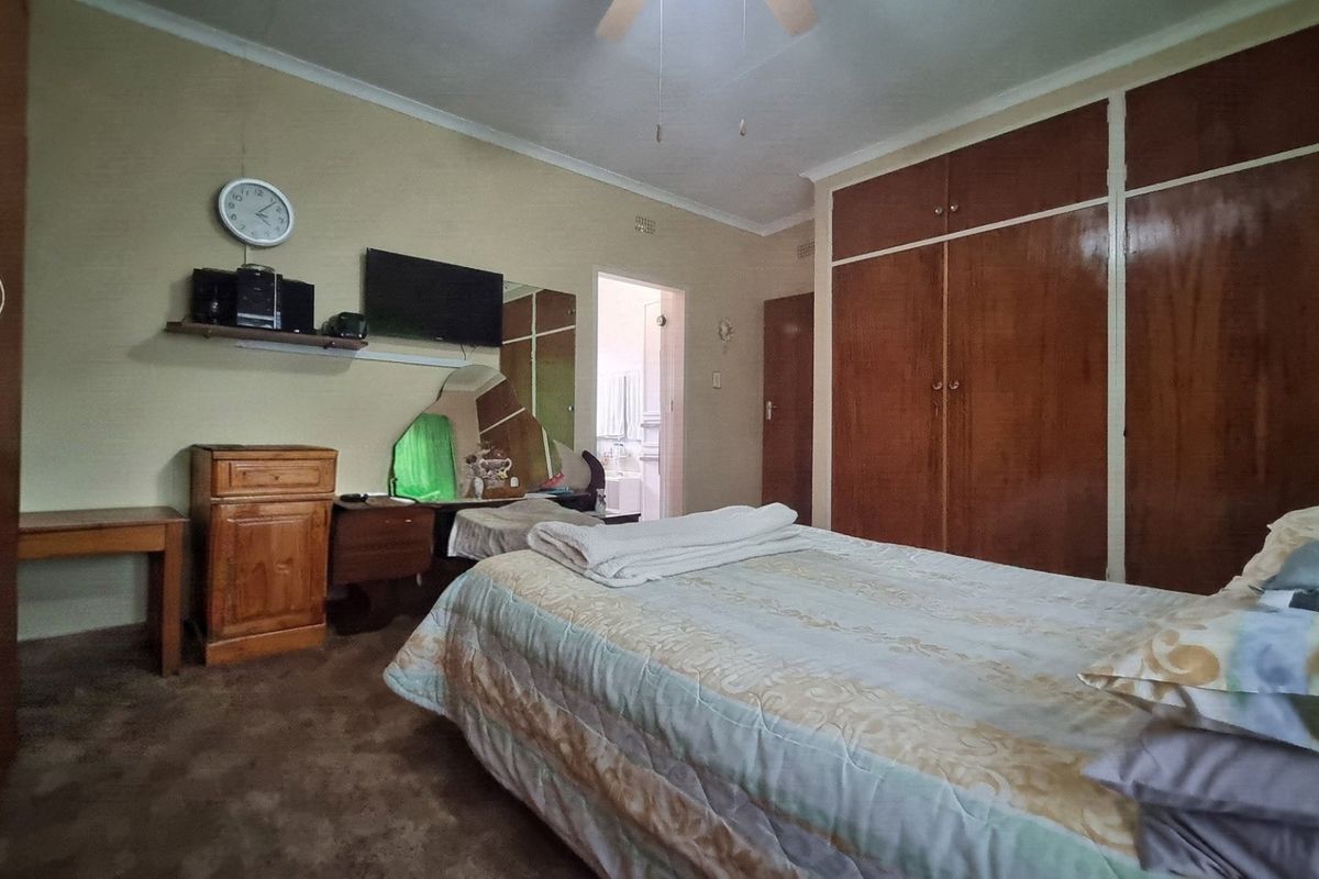 A bedroom featuring built-in wooden cupboards, a ceiling fan, and carpeted flooring, with an adjoining doorway leading to an en-suite bathroom.