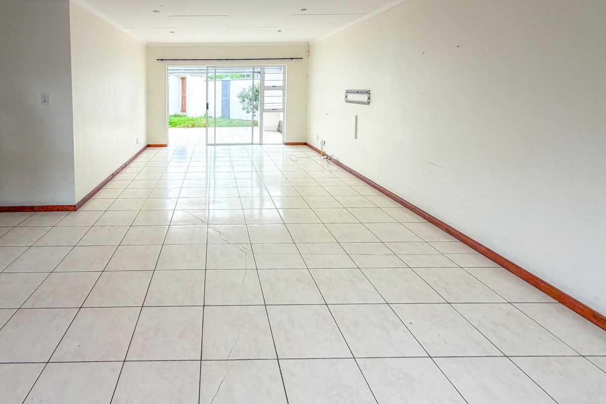 A spacious, empty living area featuring neutral tiled flooring, recessed lighting, and a sliding glass door providing direct access to the outdoor patio.
