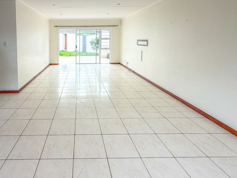 A spacious, empty living area featuring neutral tiled flooring, recessed lighting, and a sliding glass door providing direct access to the outdoor patio.
