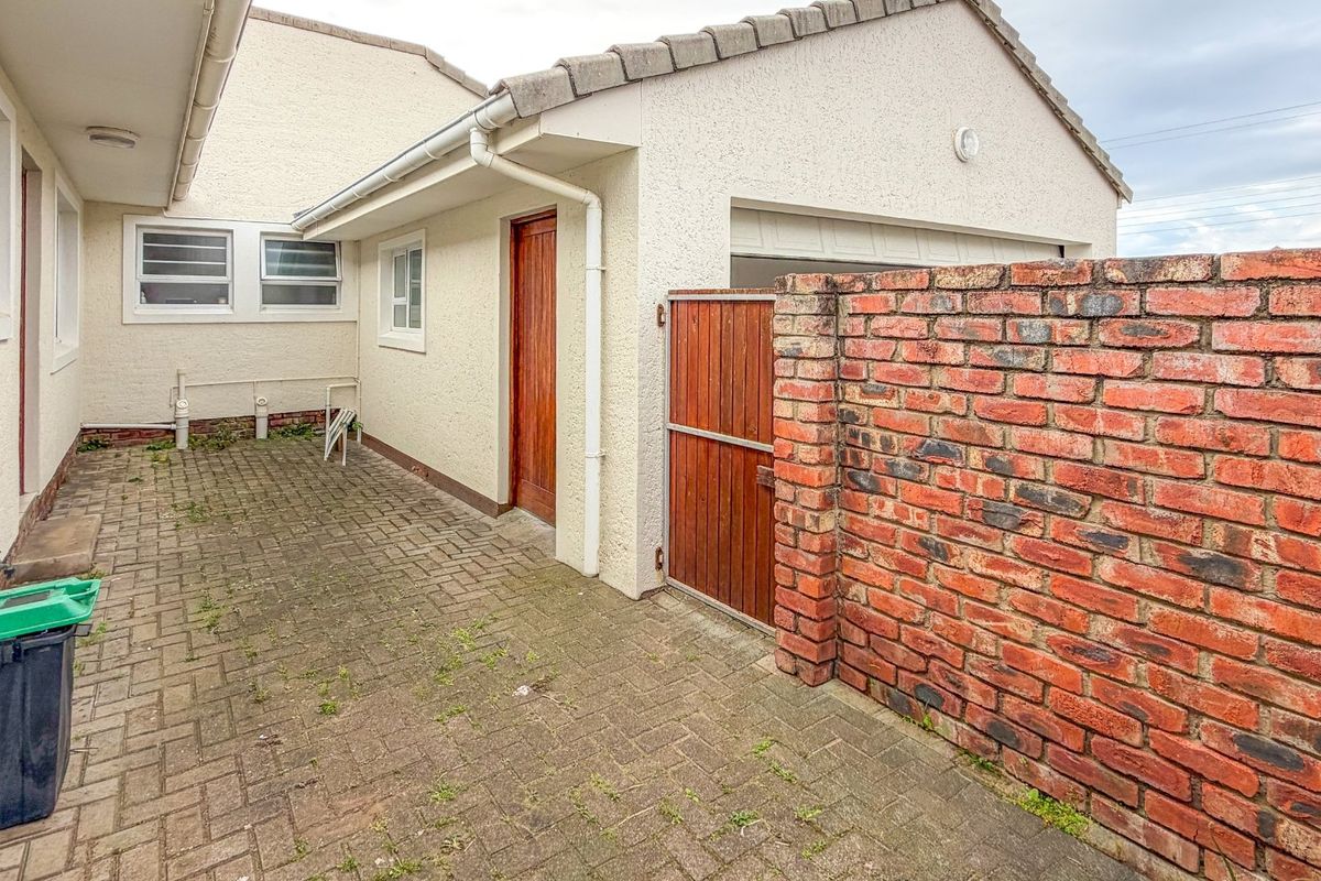 A paved rear courtyard area featuring a brick boundary wall, timber side gate, and access to the main dwelling and garage structure.