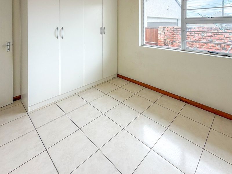 A vacant bedroom featuring neutral tiled flooring, built-in storage cupboards, and a window fitted with security bars.