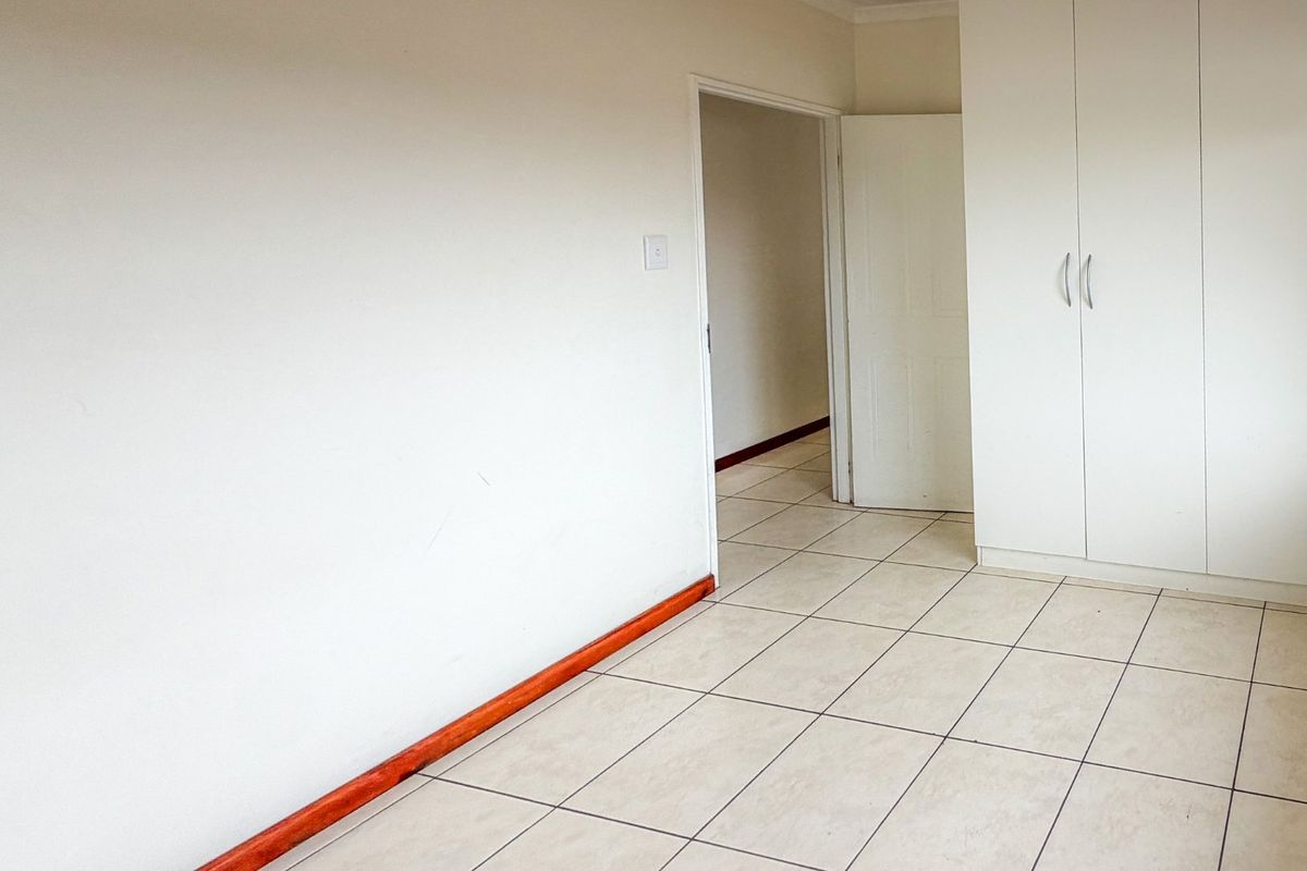 An empty bedroom featuring neutral tiled flooring, built-in cupboards, and wooden skirting boards, offering a clean and versatile space.