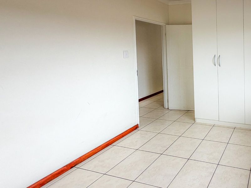 An empty bedroom featuring neutral tiled flooring, built-in cupboards, and wooden skirting boards, offering a clean and versatile space.