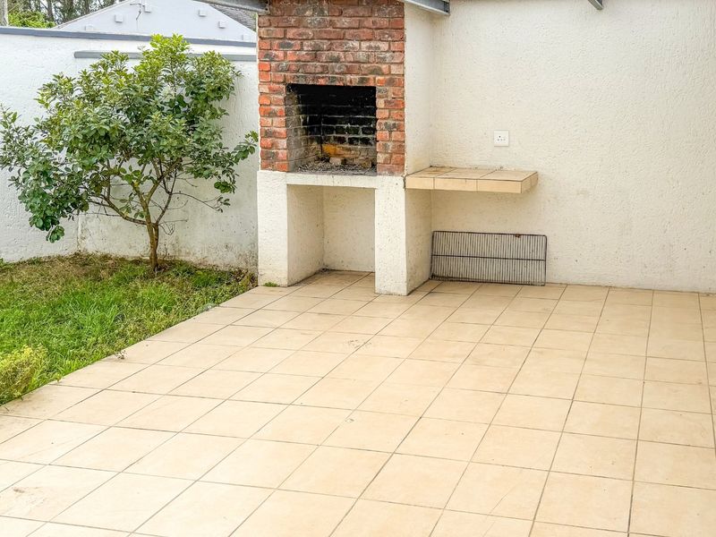 Covered patio area featuring a built-in brick braai, tiled flooring, and direct access to a small garden space.