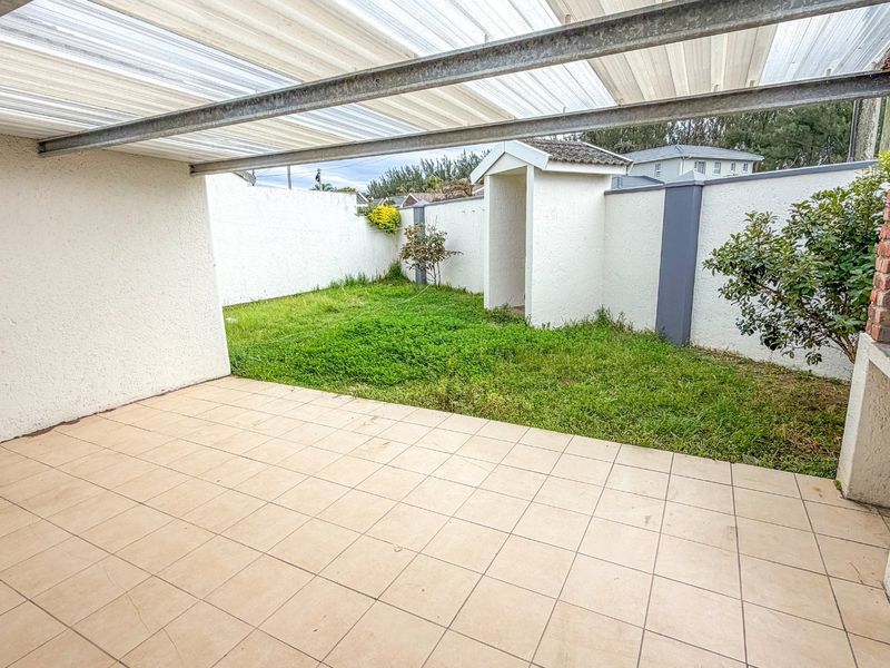 Covered patio area featuring tiled flooring and a built-in brick braai, overlooking a private garden space with perimeter walling.