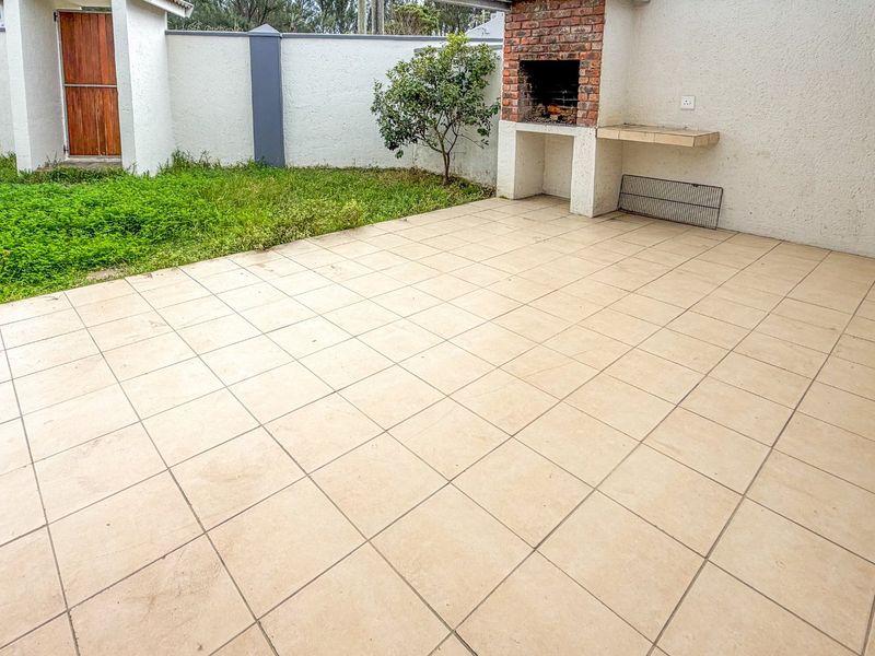 Covered patio area featuring a built-in brick braai, tiled flooring, and direct access to a small private garden space.