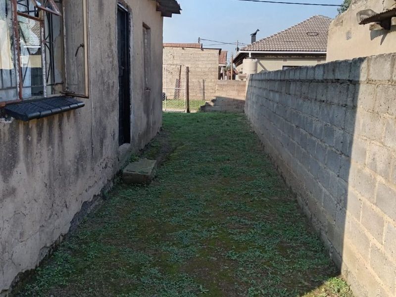 A narrow side yard area featuring a concrete block boundary wall and a weathered exterior building facade with a rusted satellite dish.