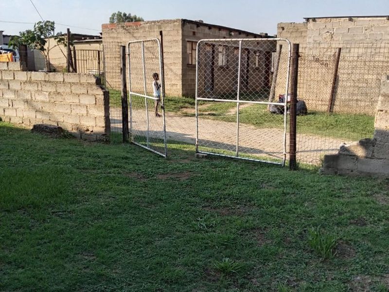 A view of the rear yard featuring a chain-link fence, metal gate, and unfinished concrete block boundary walls.