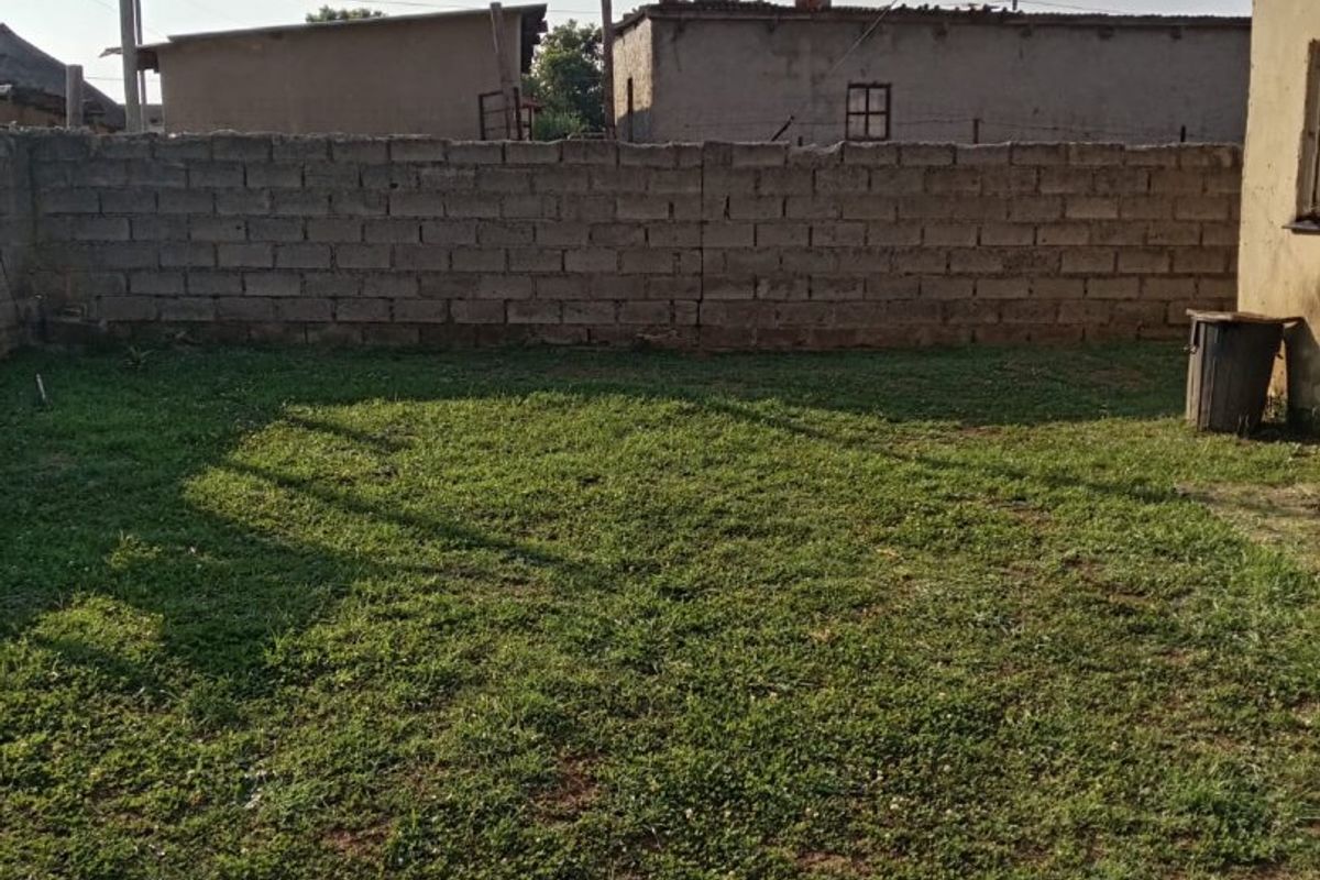 A private rear garden area featuring a grass lawn enclosed by a cinder block boundary wall.