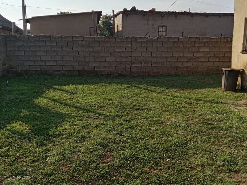 A private rear garden area featuring a grass lawn enclosed by a cinder block boundary wall.