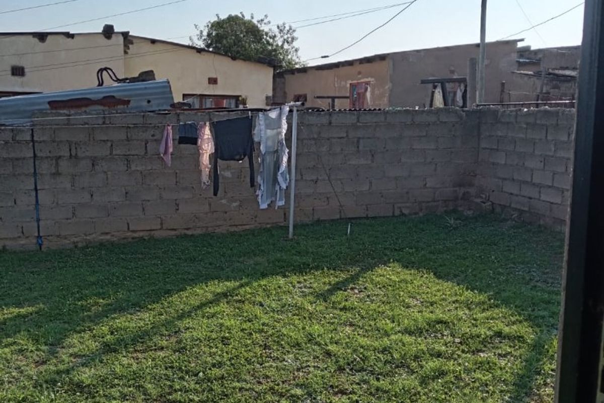 A rear yard featuring a grass lawn enclosed by a concrete block boundary wall.
