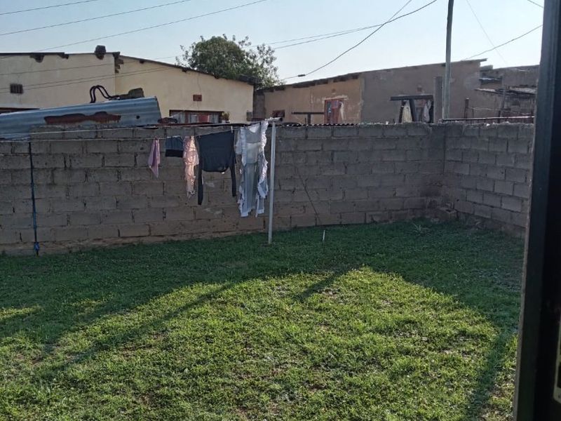 A rear yard featuring a grass lawn enclosed by a concrete block boundary wall.