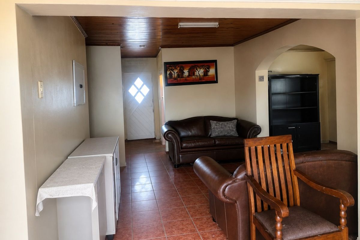 A living area featuring tiled flooring, a timber-paneled ceiling, and a decorative archway leading to an entrance with a glass-paneled door.