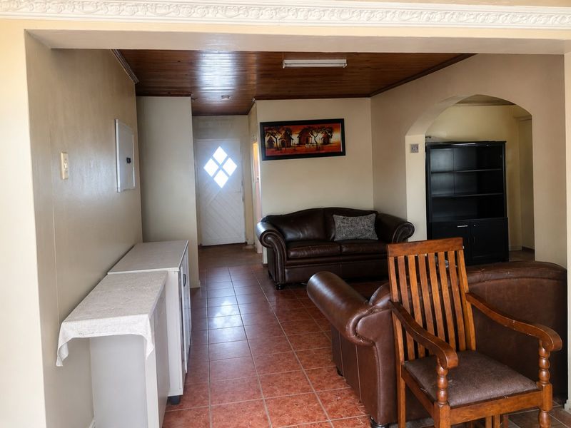 A living area featuring tiled flooring, a timber-paneled ceiling, and a decorative archway leading to an entrance with a glass-paneled door.