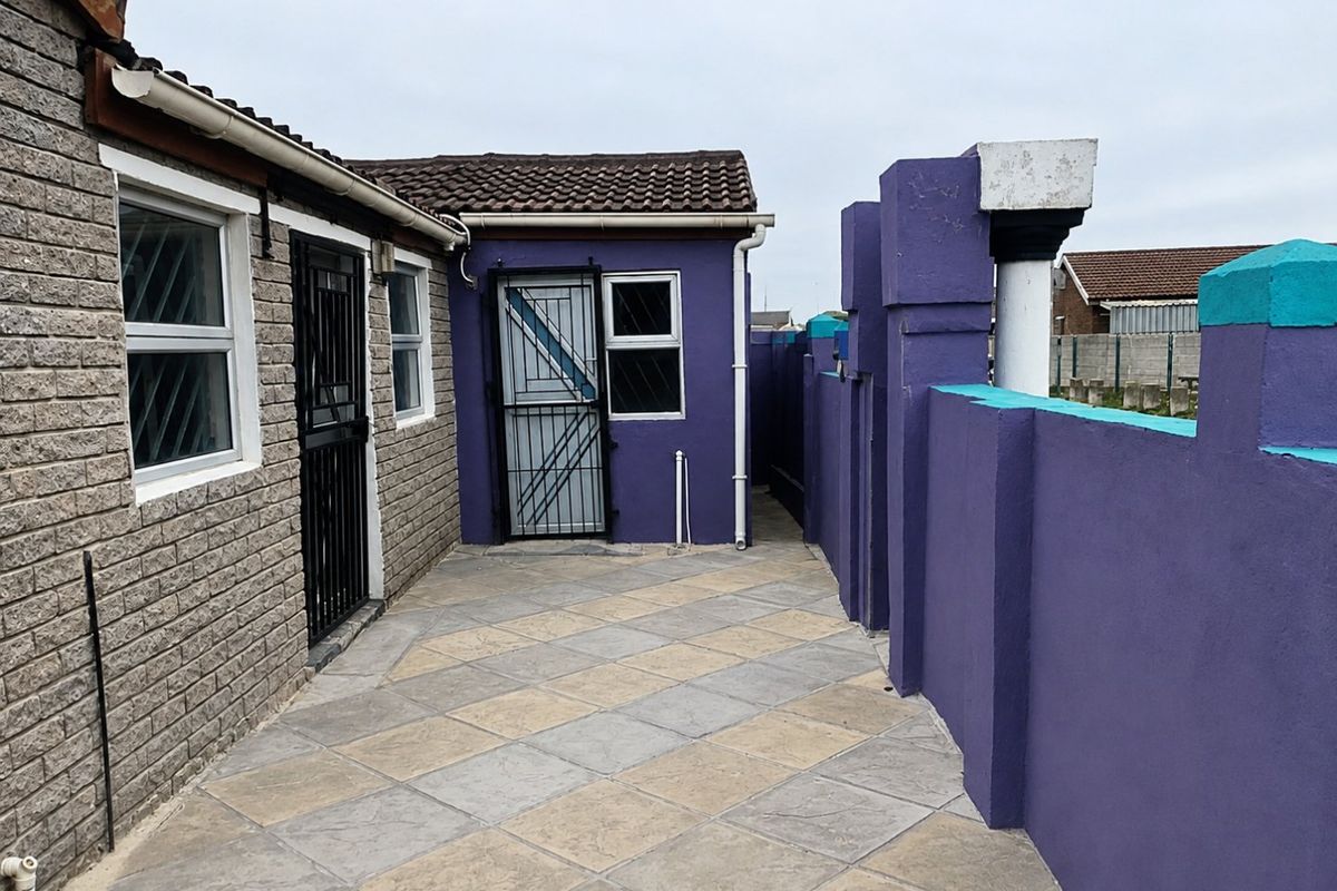 Rear exterior area featuring a paved patio, security gates, and a painted boundary wall with concrete roof tiles.