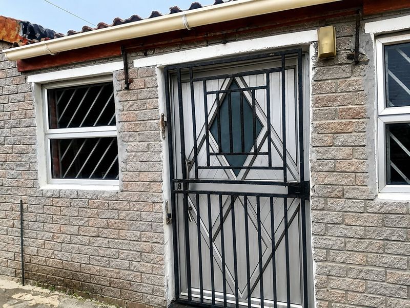 Exterior view of a brick-built entrance featuring a security gate and window security bars, showing signs of age and weathering.