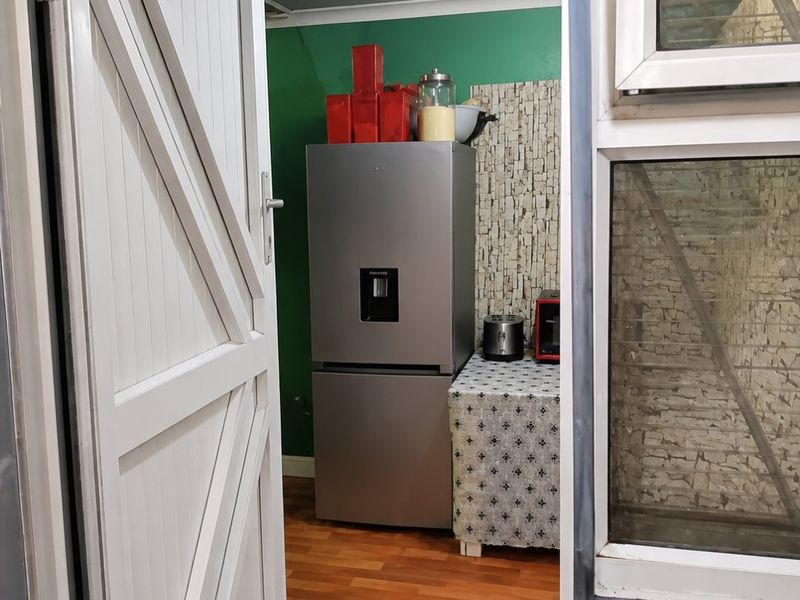 A functional scullery or utility area featuring laminate flooring and a tiled splashback, viewed through a doorway.