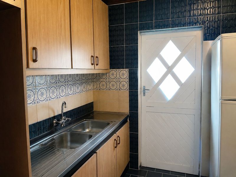 A functional kitchen area featuring wood-finish cabinetry, a stainless steel double sink, and decorative tiled backsplash with direct access to the exterior.