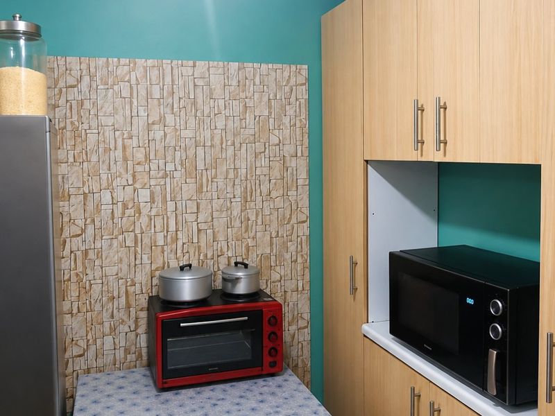 A functional kitchen area featuring light wood-tone built-in cabinetry, a textured stone-look feature wall, and a dedicated microwave nook.