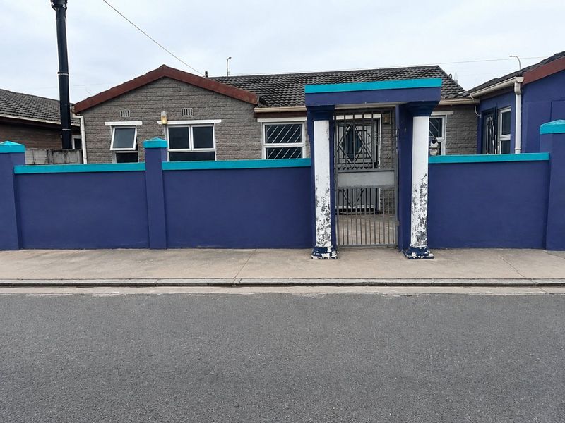 Front elevation of a residential property featuring a boundary wall with decorative pillars, a security gate, and a tiled roof.
