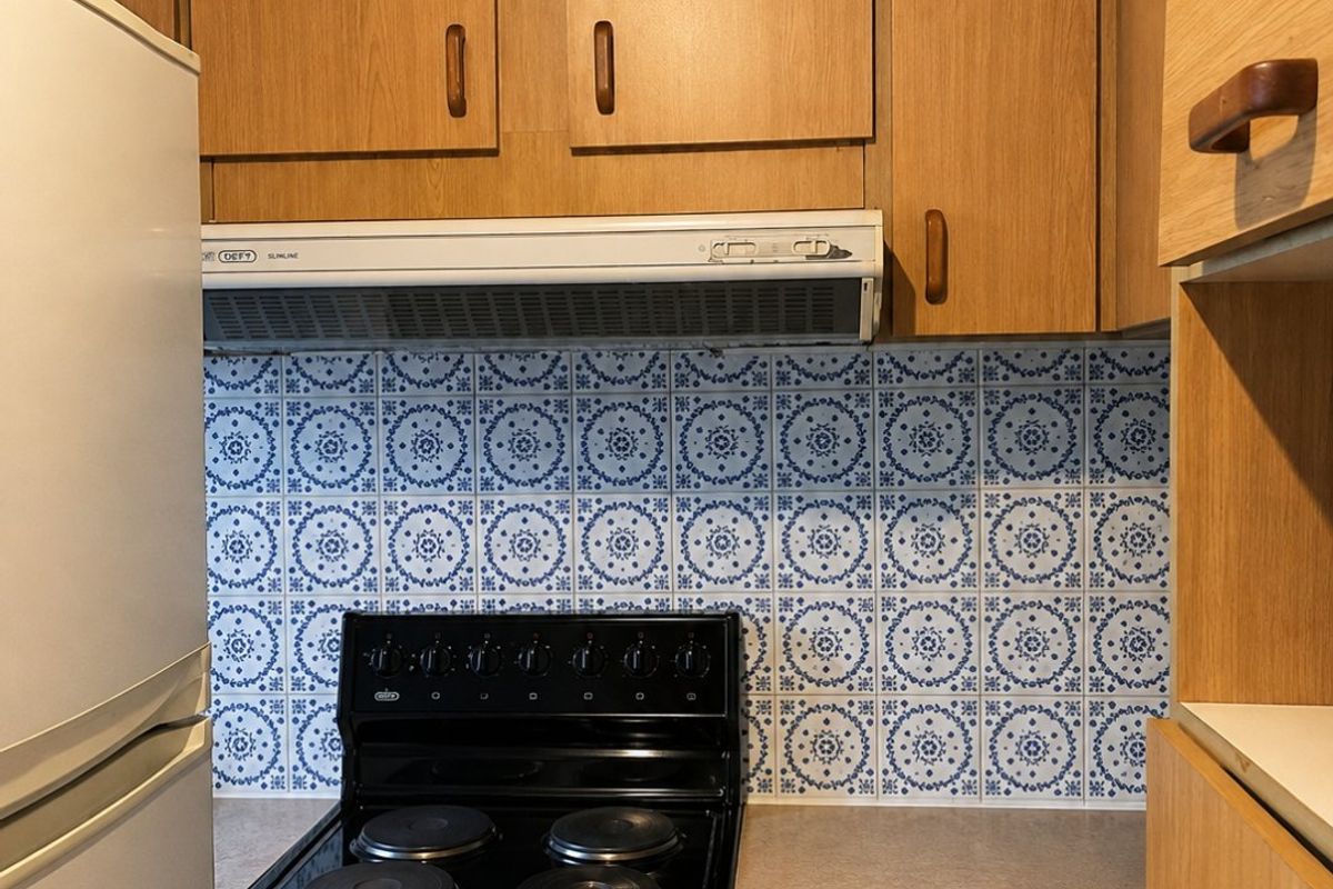A functional kitchen featuring wooden cabinetry, a patterned tile backsplash, and a built-in electric stove with an extractor fan.