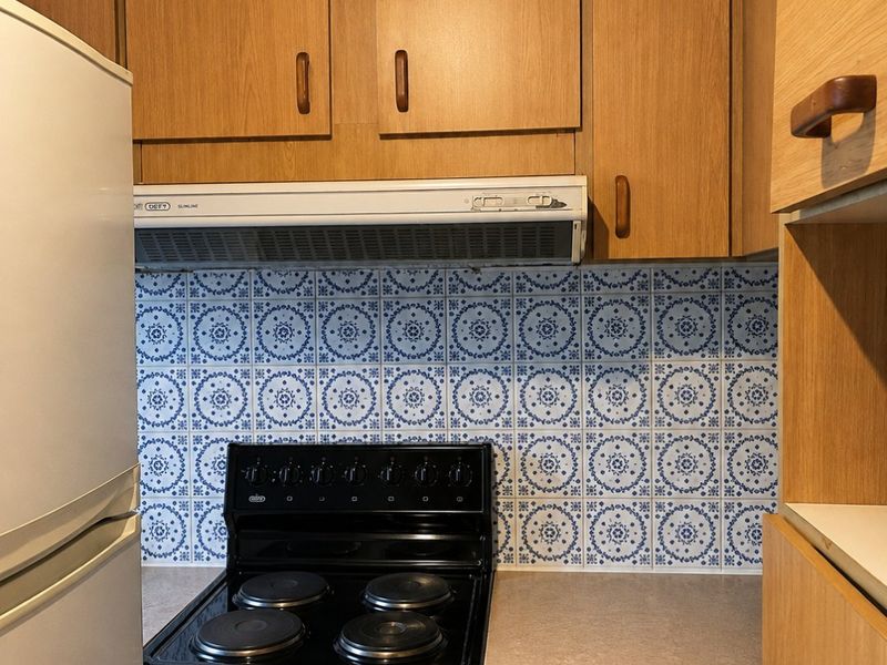 A functional kitchen featuring wooden cabinetry, a patterned tile backsplash, and a built-in electric stove with an extractor fan.
