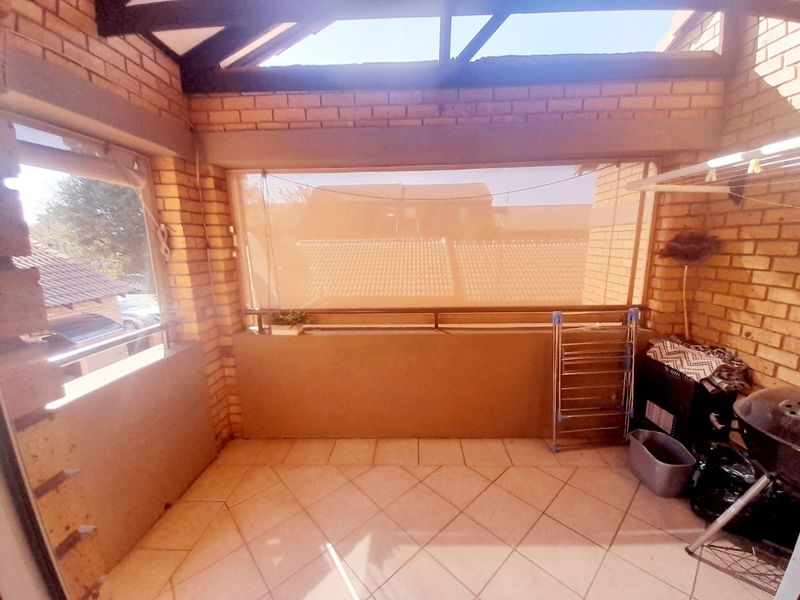 A covered balcony featuring exposed brick walls, tiled flooring, and timber rafters, equipped with a retractable outdoor blind and metal balustrade.