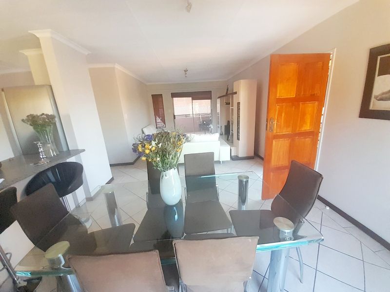 Open-plan living and dining area featuring tiled flooring, a breakfast counter, and access to an outdoor balcony through sliding glass doors.