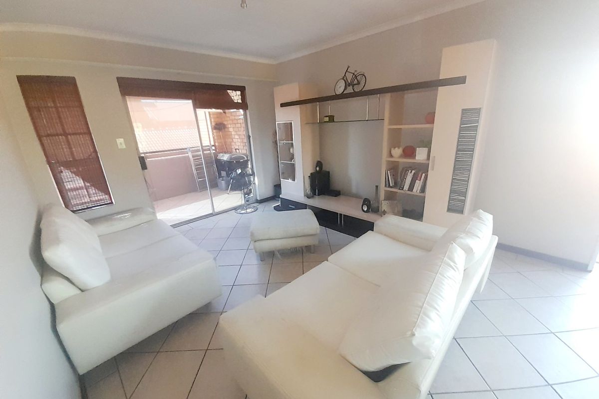 A living room featuring tiled flooring, a built-in shelving unit, and a sliding glass door providing access to an outdoor patio area.