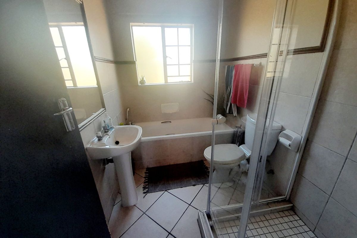A functional bathroom featuring a pedestal basin, built-in bathtub, and a separate glass-enclosed shower with tiled finishes throughout.