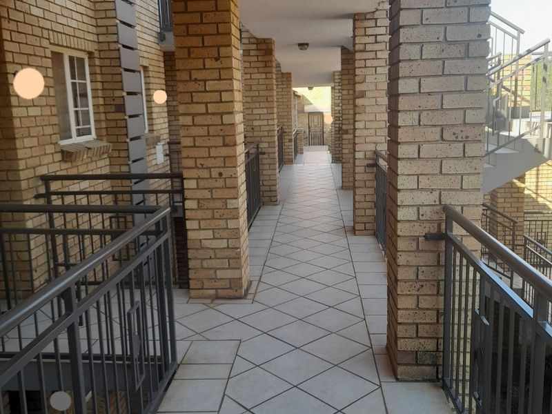 An exterior apartment hallway featuring brick columns, tiled flooring, and metal safety railings.