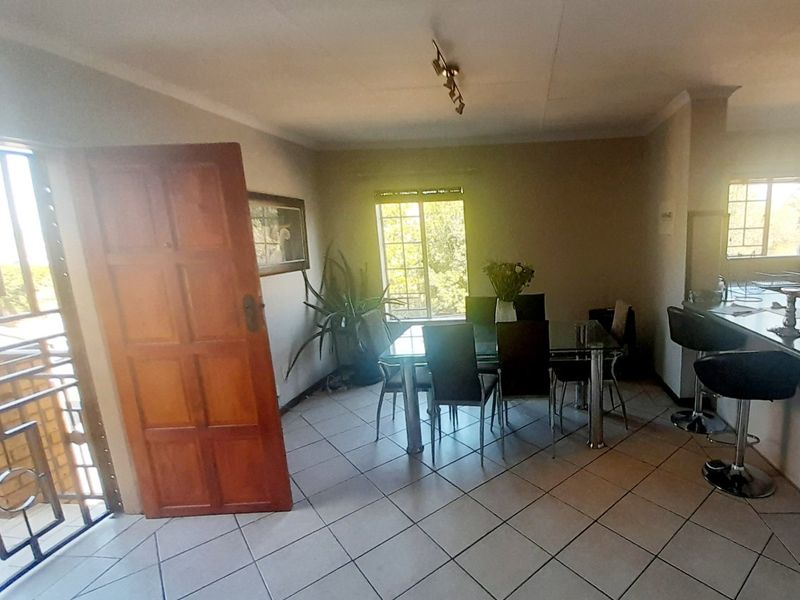 Open plan living and dining area featuring tiled flooring, a breakfast bar, and direct access to an outdoor balcony through a security gate.