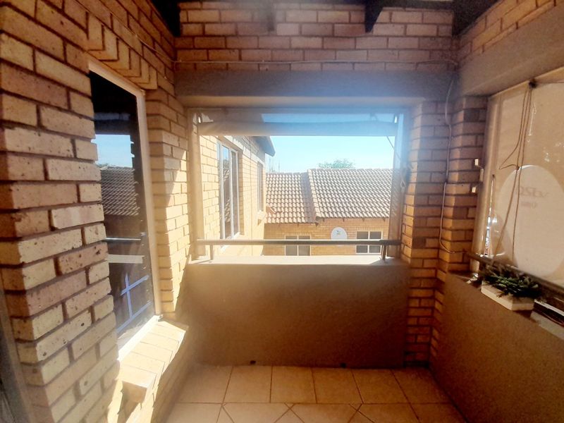 A covered balcony featuring exposed brick walls, tiled flooring, and a metal balustrade, offering a functional outdoor space.