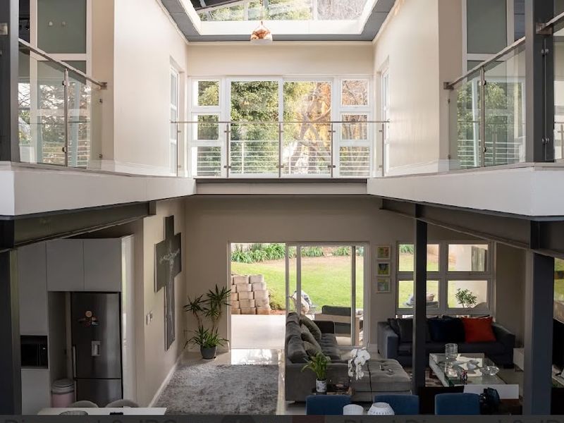 Spacious open-plan living area featuring a double-volume ceiling with a large skylight, mezzanine level with glass balustrades, and direct access to the garden.